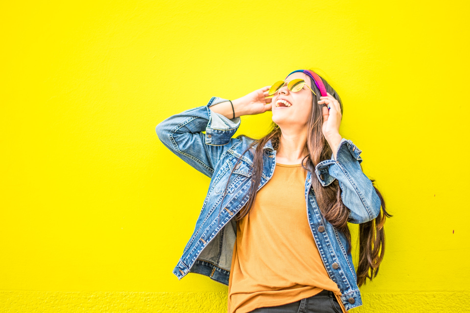 Laughing girl in modern clothing with yellow wall behind